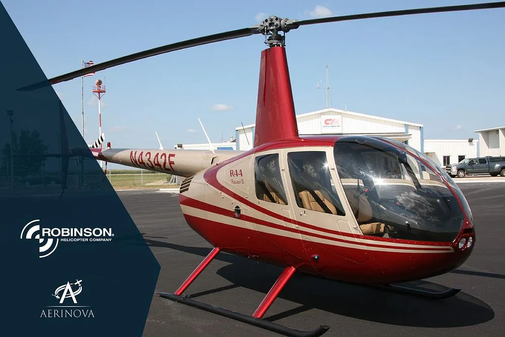 A red and tan Robinson R44 Raven II helicopter (N4342F) is parked on an asphalt apron with hangars in the background.