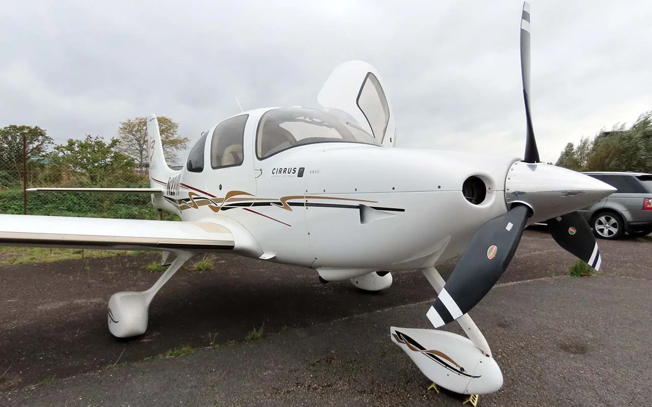 A front-quarter view of a white Cirrus SR22T (N224RC) with its doors open, parked on an asphalt surface.