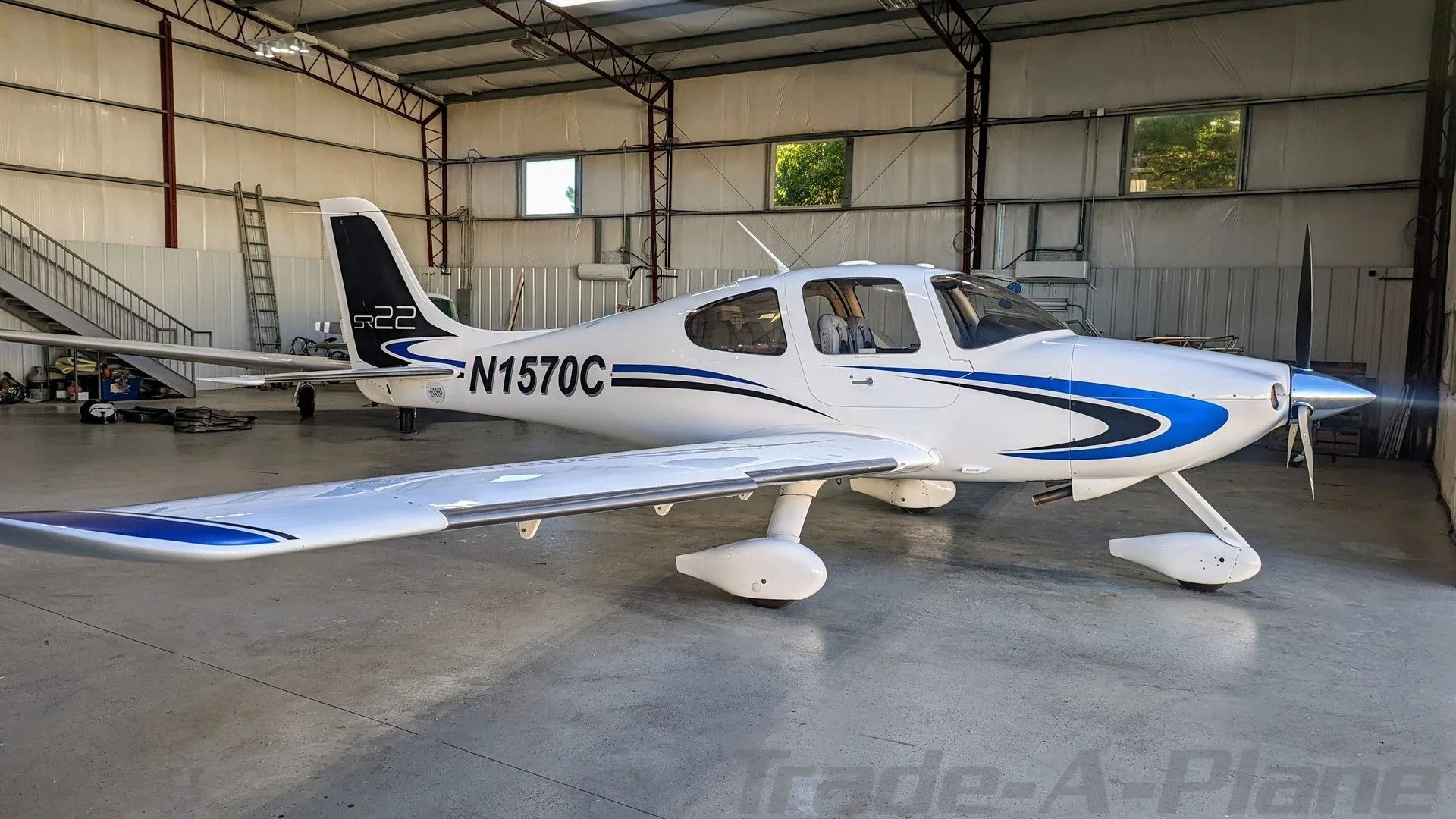 A white Cirrus SR22 aircraft with blue and black stripes, registration N1570C, parked inside a hangar.