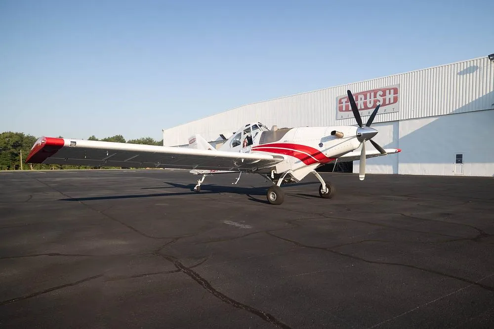 A white and red Thrush 510G aircraft parked on an asphalt tarmac in front of a white hangar with the 'THRUSH AIRCRAFT' logo.