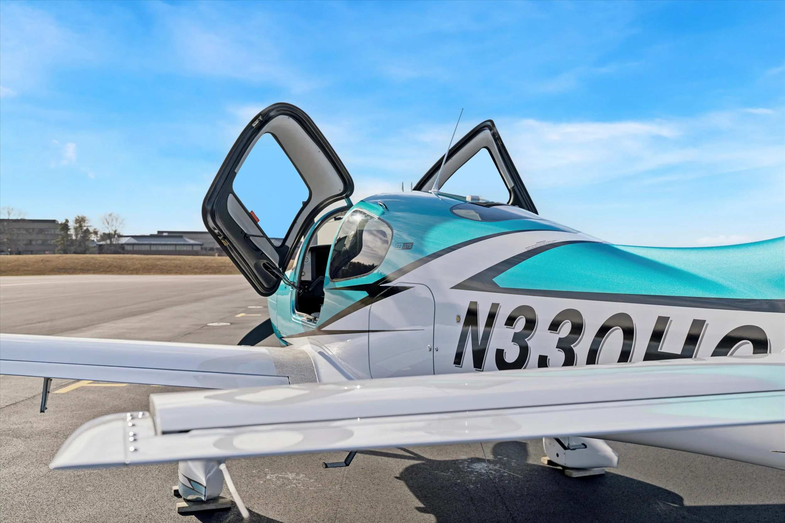 A side view of a teal and white Cirrus SR22 aircraft, registration N330HC, with both gull-wing doors open on an airfield.