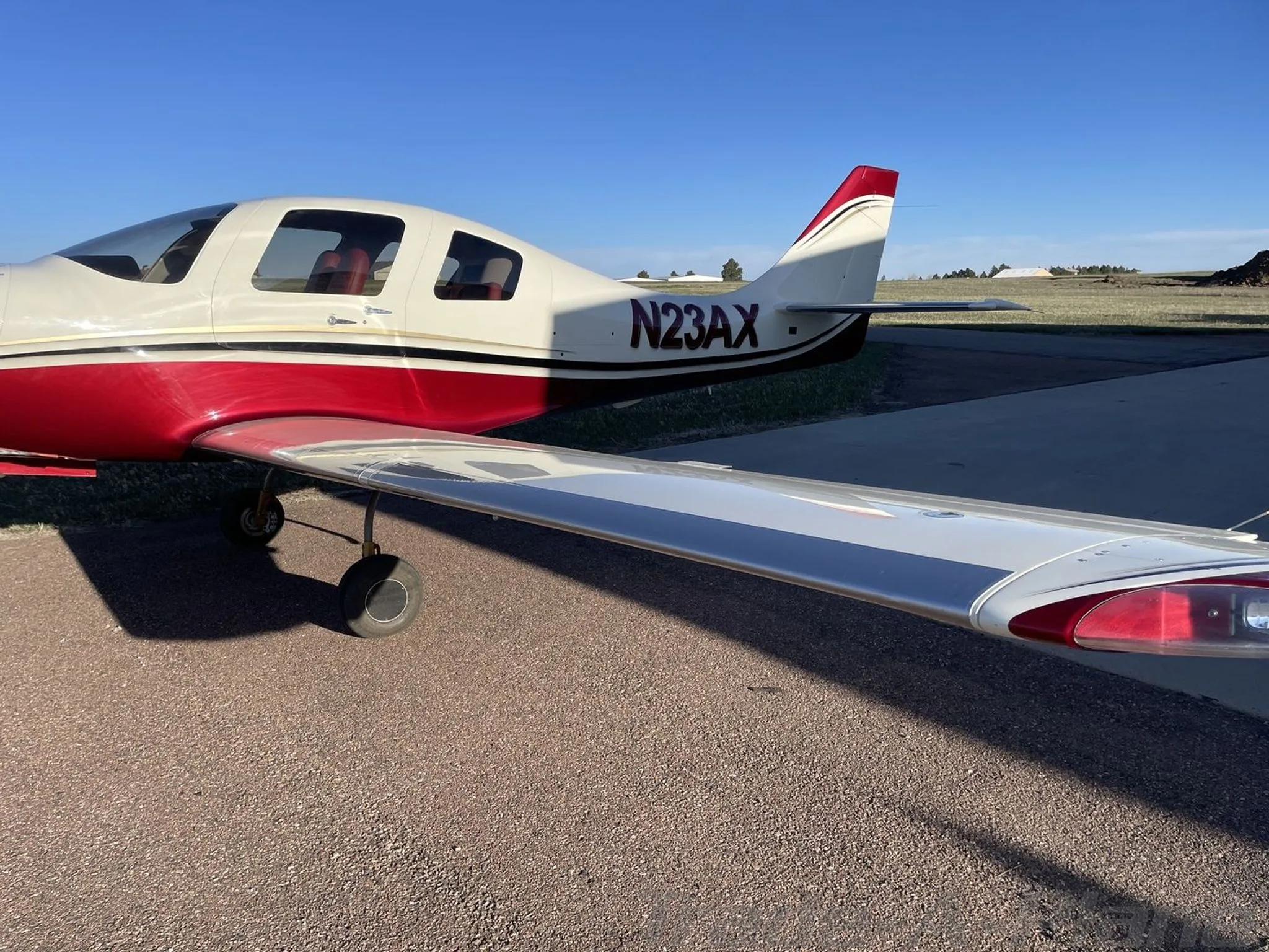 A close-up side view of the white and red aircraft N23AX, showing its wing and tail on a paved surface.