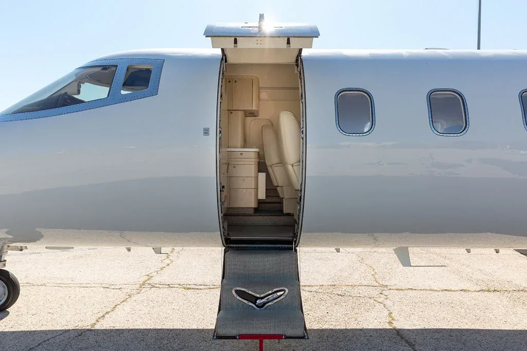 The open main entry door of a white Learjet business jet, revealing the steps and a glimpse of the cabin interior.