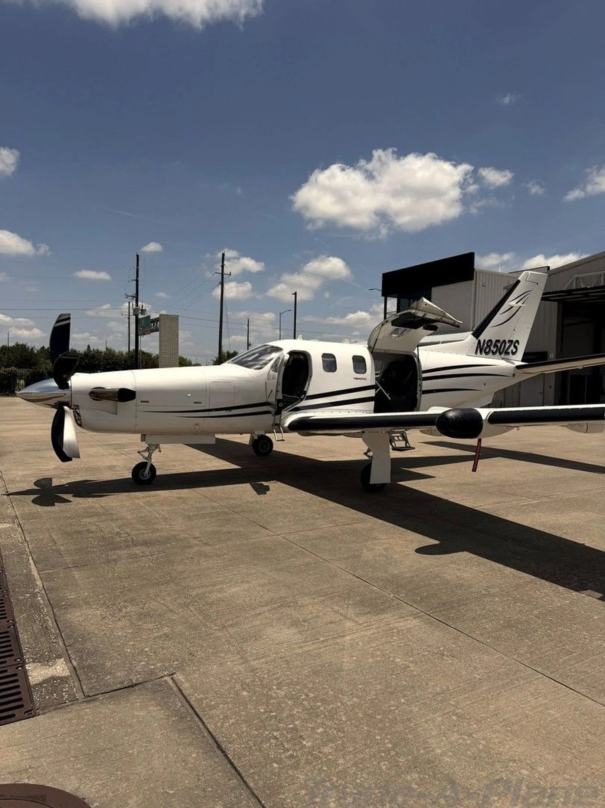 A white turboprop aircraft with black stripes and registration N850ZS parked with its cabin doors open.