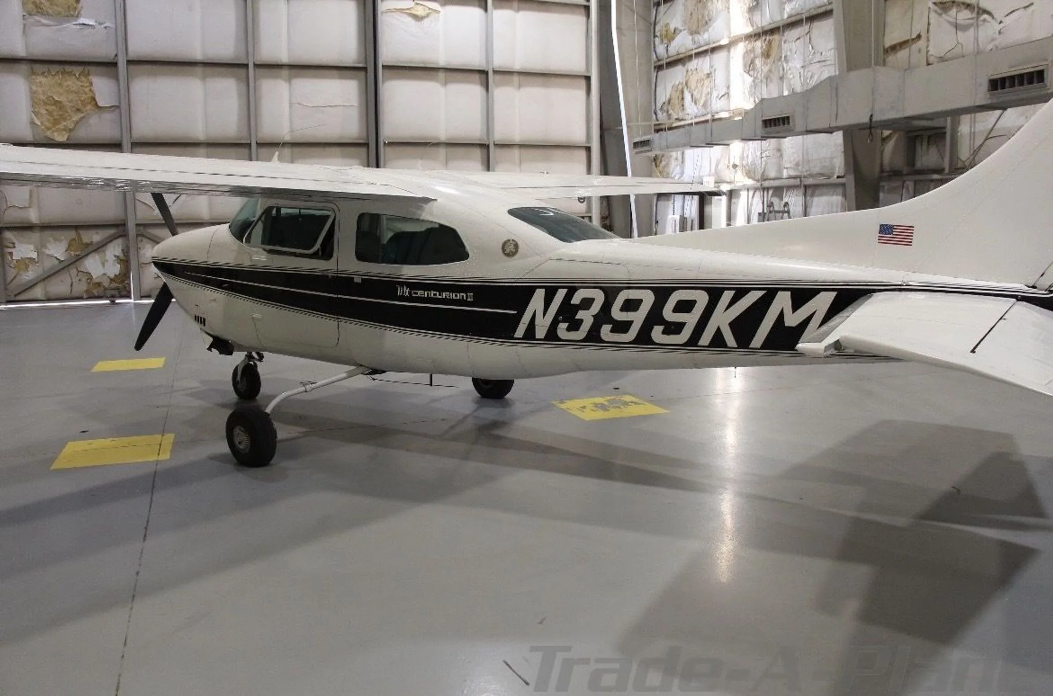 A white Cessna 210 Centurion with black stripes, showing the rear fuselage and tail, in a hangar.