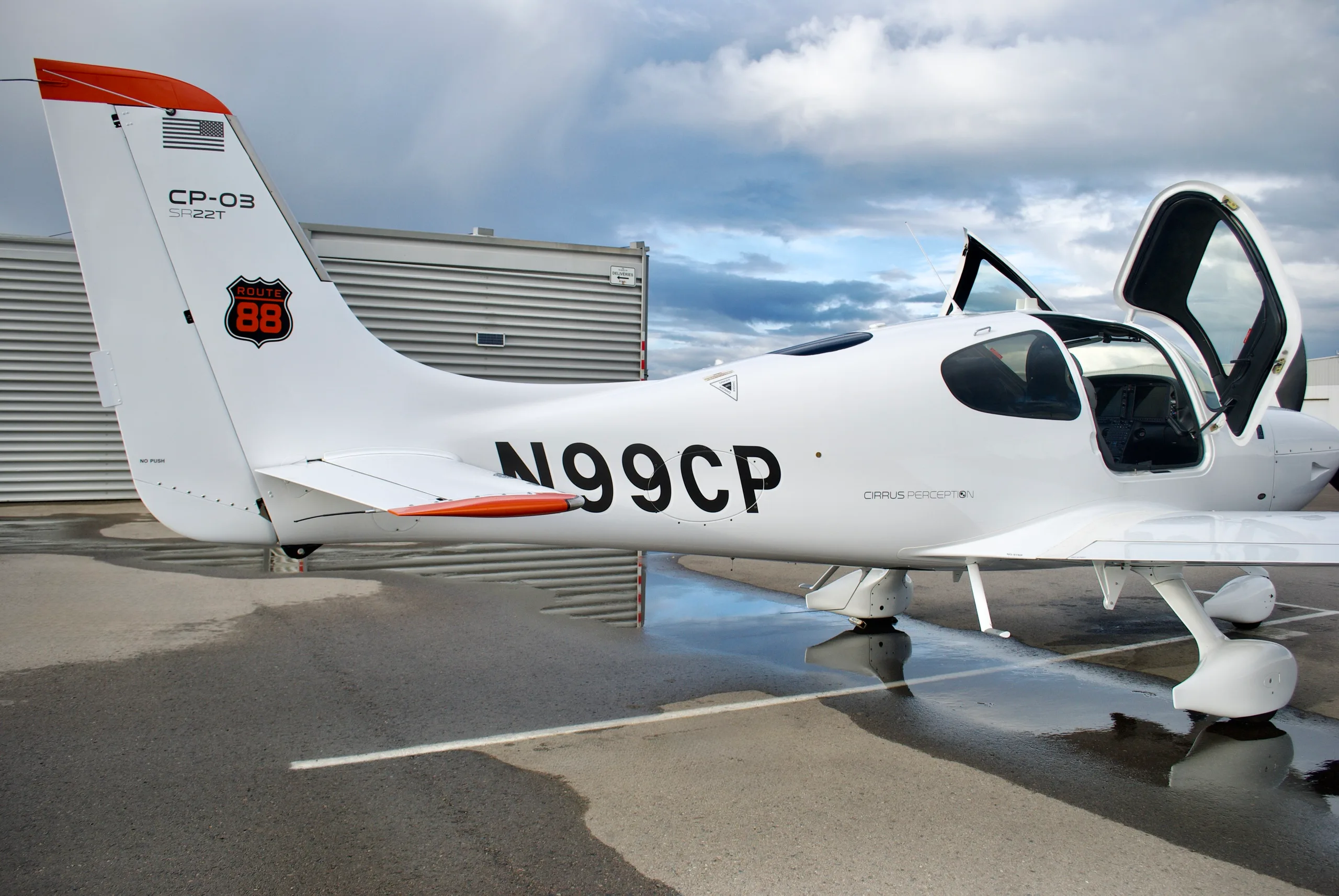 The rear-left side of a white Cirrus SR22T aircraft with registration N99CP, showing the tail with a "ROUTE 88" logo and an open door.