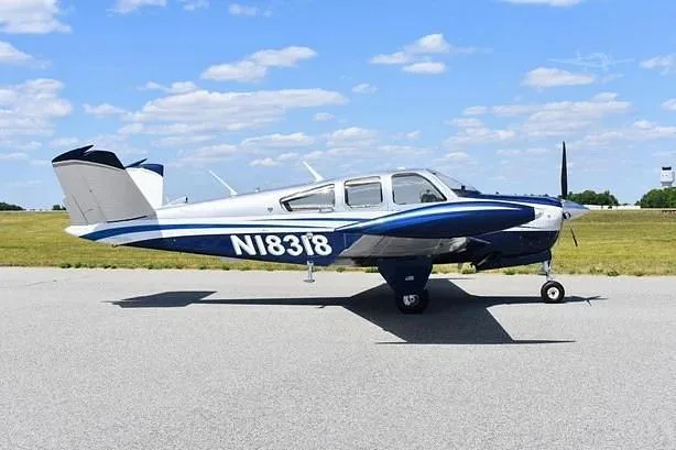 A side view of a white and blue single-engine propeller aircraft with registration N18318 on an airfield.