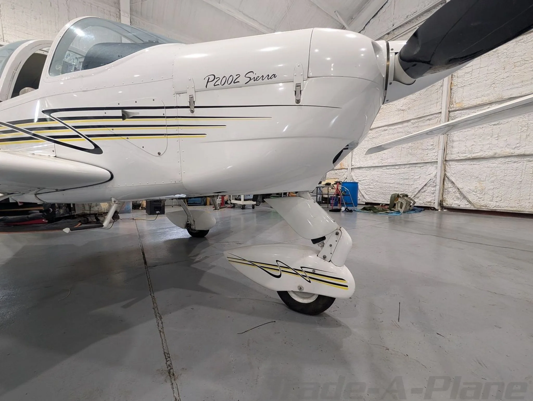 A close-up of the nose and front landing gear of the white Tecnam P2002 Sierra, showing its black and yellow stripe paint scheme.