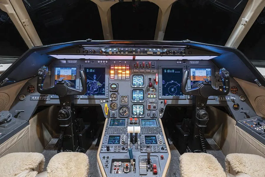 The cockpit of a private jet, featuring multiple digital displays, instrument panels, and control yokes.