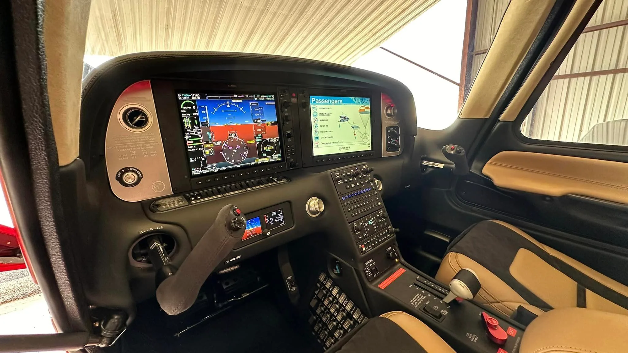 A detailed view of the modern glass cockpit of a Cirrus SR22 aircraft, featuring dual large display screens and a side stick control.