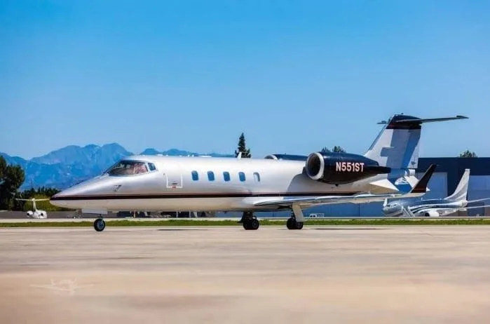 A Learjet N551ST on the tarmac with mountains in the background.