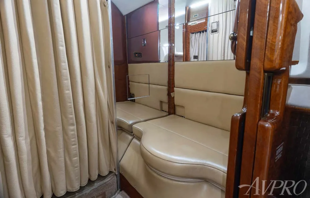 A private jet's interior shows a beige curtain, bench seating, and polished wood accents.