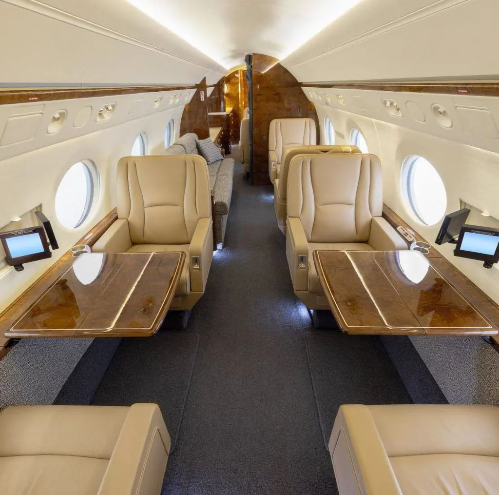 The luxurious cabin interior of a business jet with tan leather seats and polished wood tables.