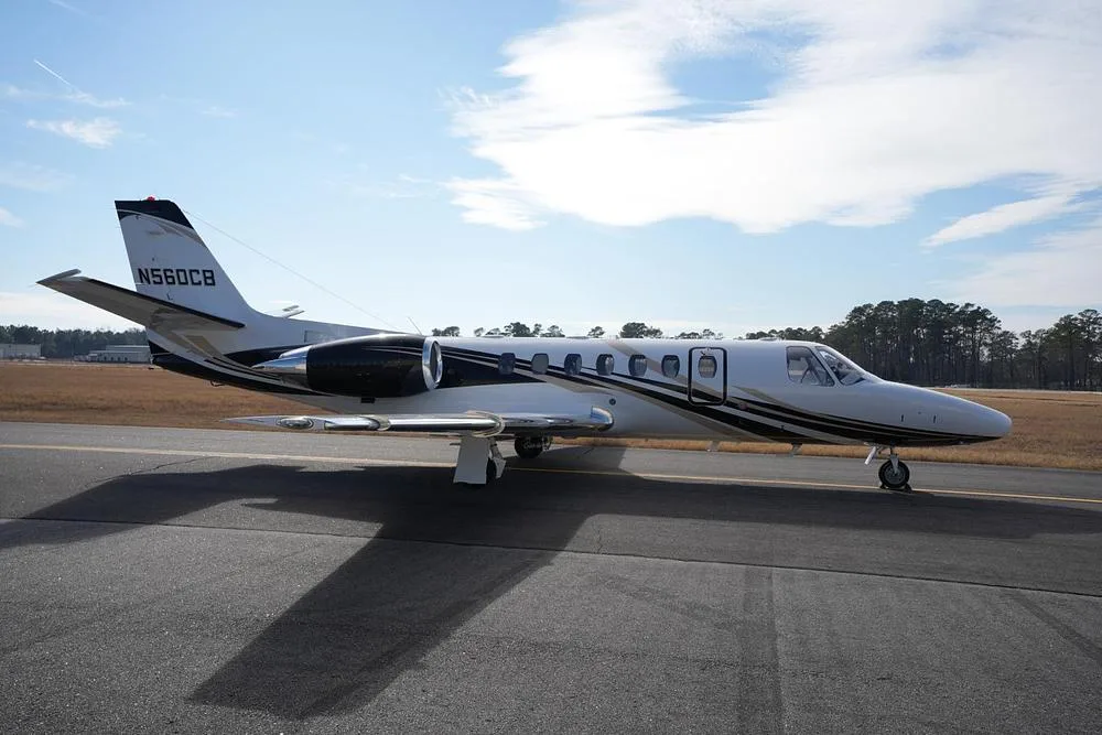 The Cessna Citation Encore business jet N560CB, featuring a white body with black and gold accent stripes, parked on an airfield.