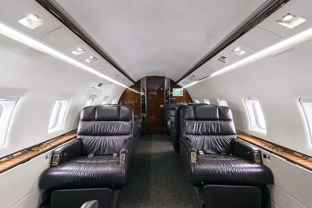 The luxurious interior cabin of a private jet, featuring black leather seats and wood paneling.