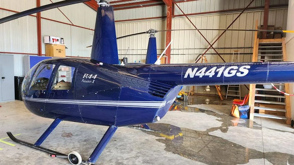 The side view of a dark blue Robinson R44 Raven I helicopter with registration N441GS in a hangar.