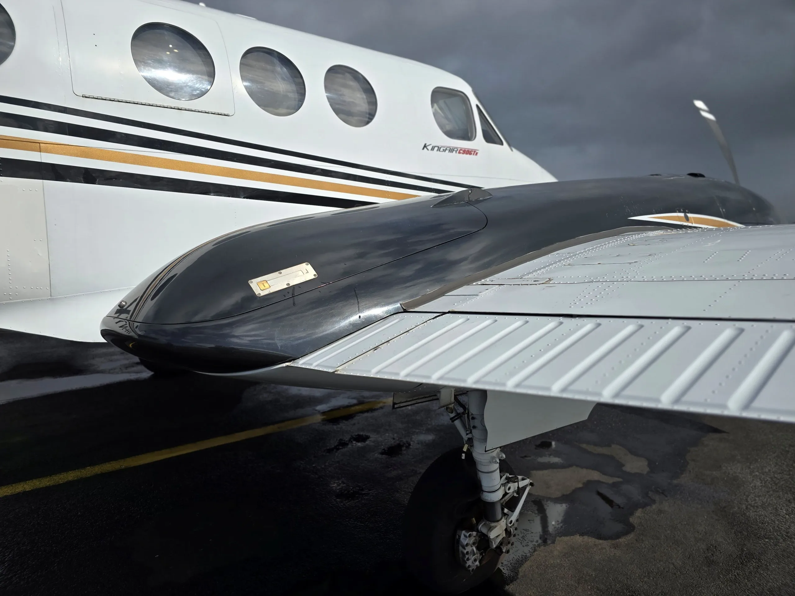 A close-up view of the wing and fuselage of a white and black Beechcraft King Air on a wet tarmac.