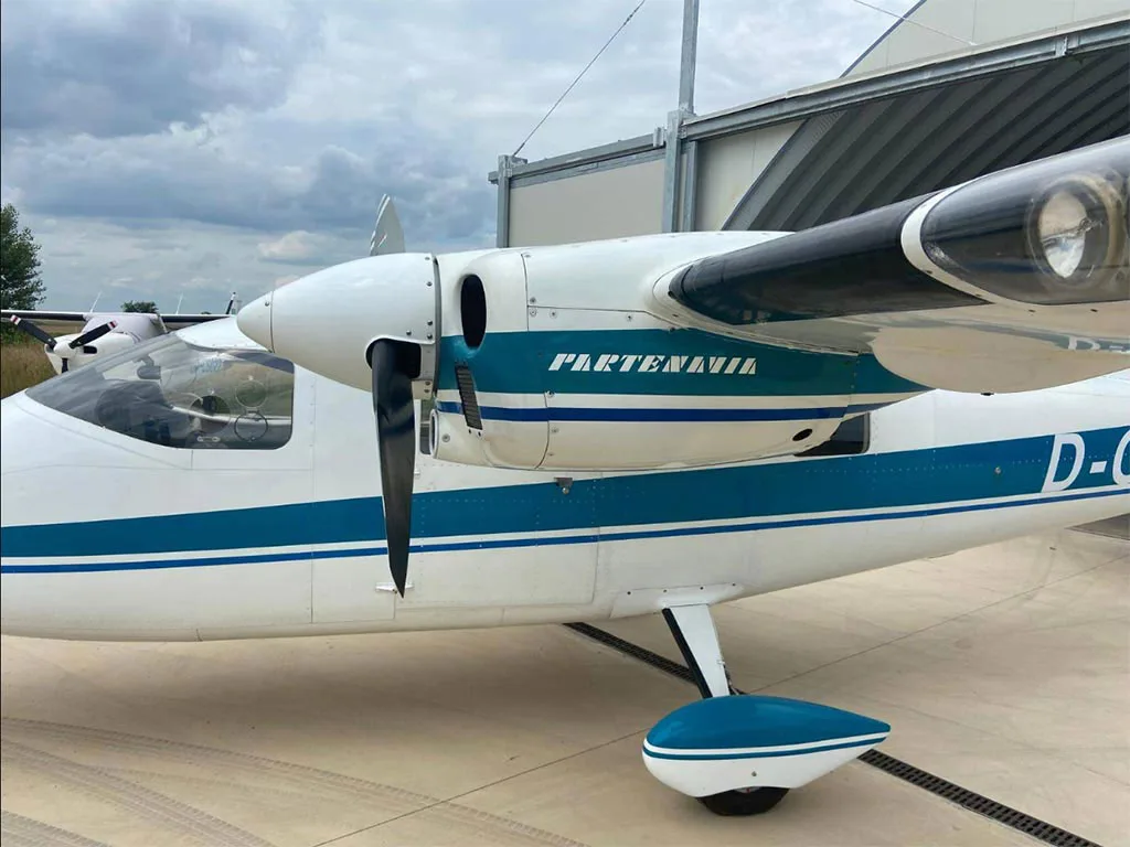 A close-up view of the front left side of a white and blue Partenavia P.68 aircraft, showing the cockpit and engine nacelle.