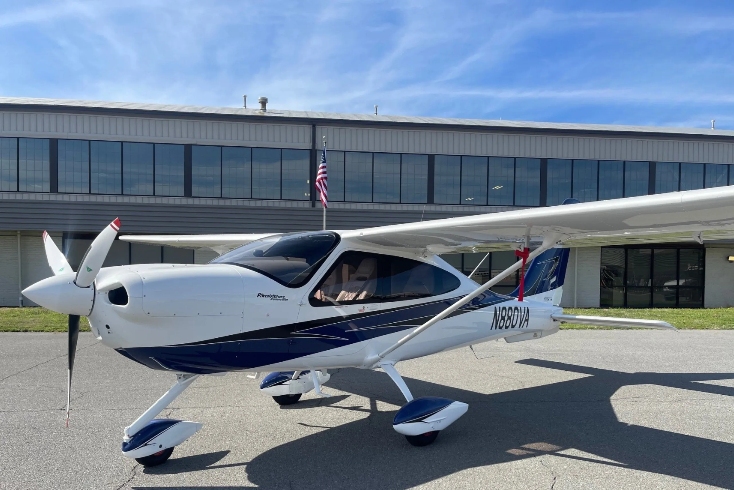 A white and blue aircraft parked in front of a building with an American flag.