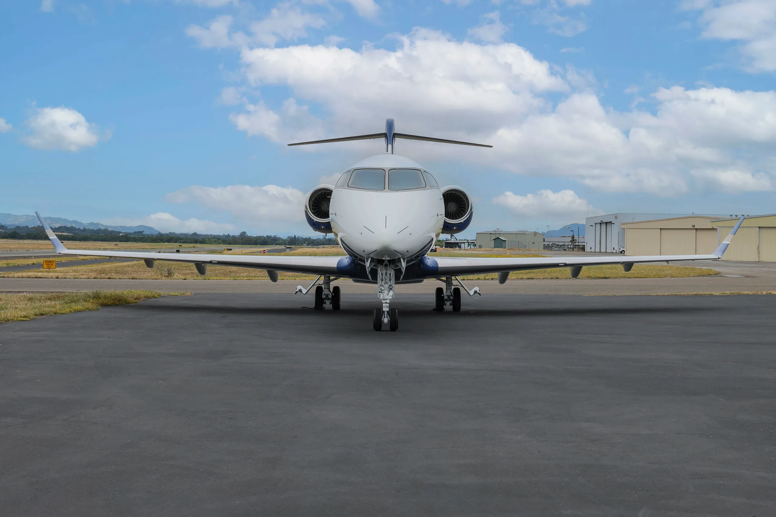 A head-on view of a Bombardier Challenger 350 business jet with white and blue paint scheme parked on an airport tarmac.