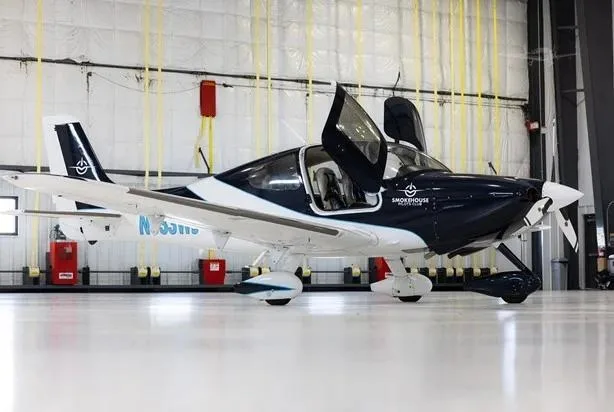 A dark blue and white single-engine aircraft N333WS with its gull-wing doors open, parked in a hangar.