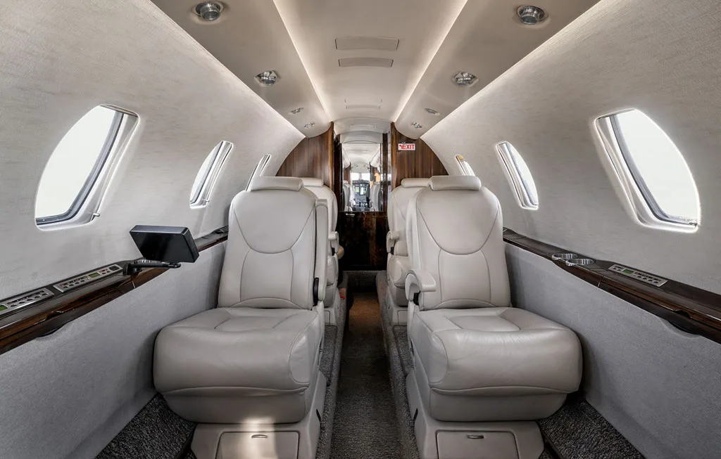 The luxurious cabin interior of the business jet features light-colored leather seats and a central aisle.