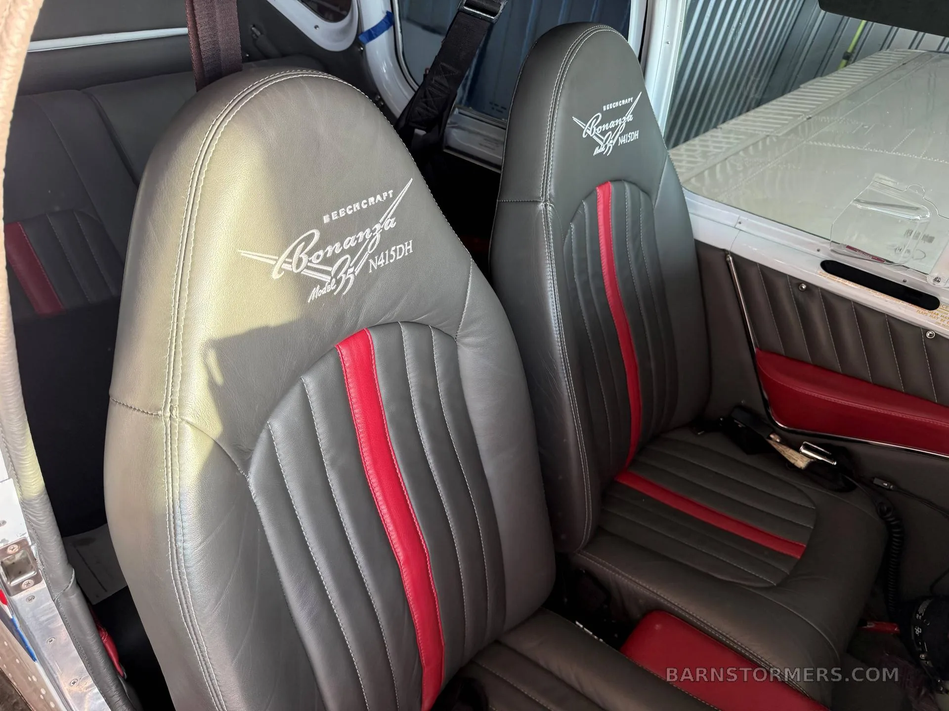 The gray leather interior seats of a Beechcraft Bonanza N415DH with red accents and embroidered logos.