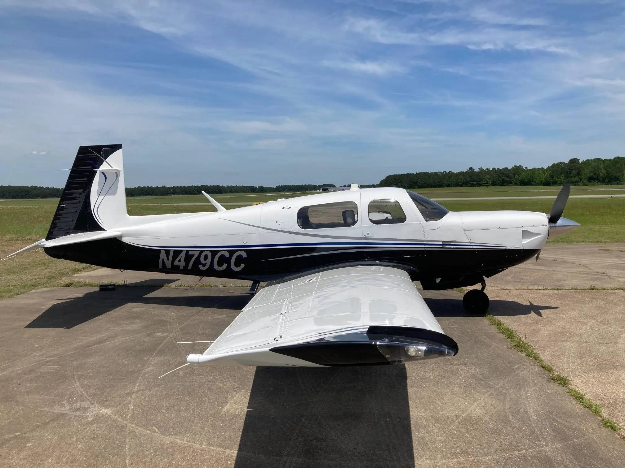 A white and black single-engine propeller aircraft, N479CC, is parked on a tarmac under a blue sky.