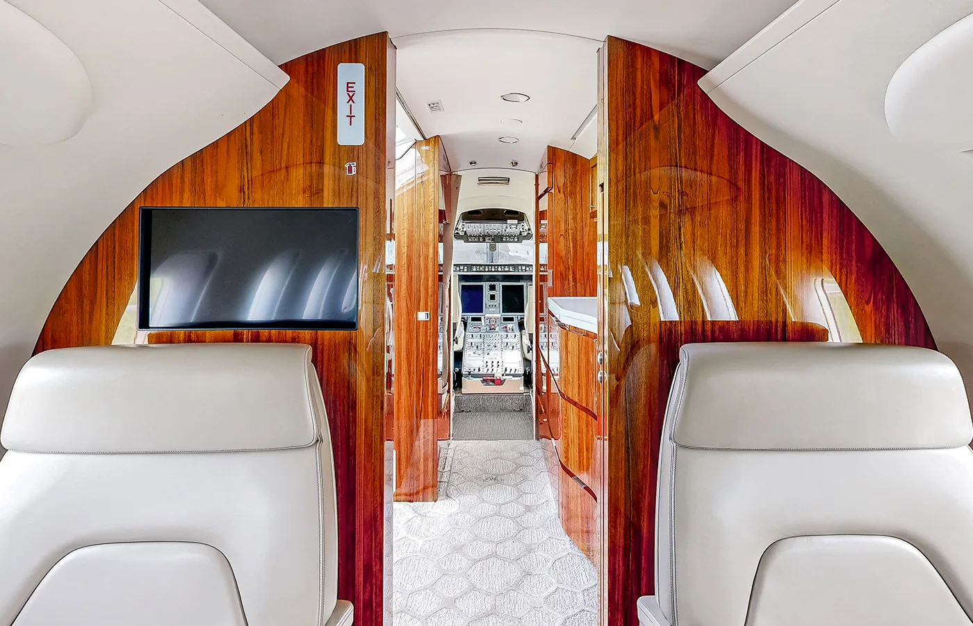 The private jet cabin interior features elegant wooden paneling, an 'EXIT' sign, and a view towards the cockpit.