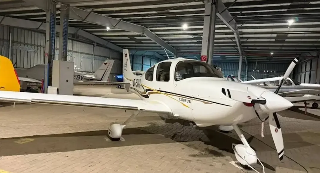 A white Cirrus SR22 aircraft with gold and black stripes parked inside a hangar with other planes.