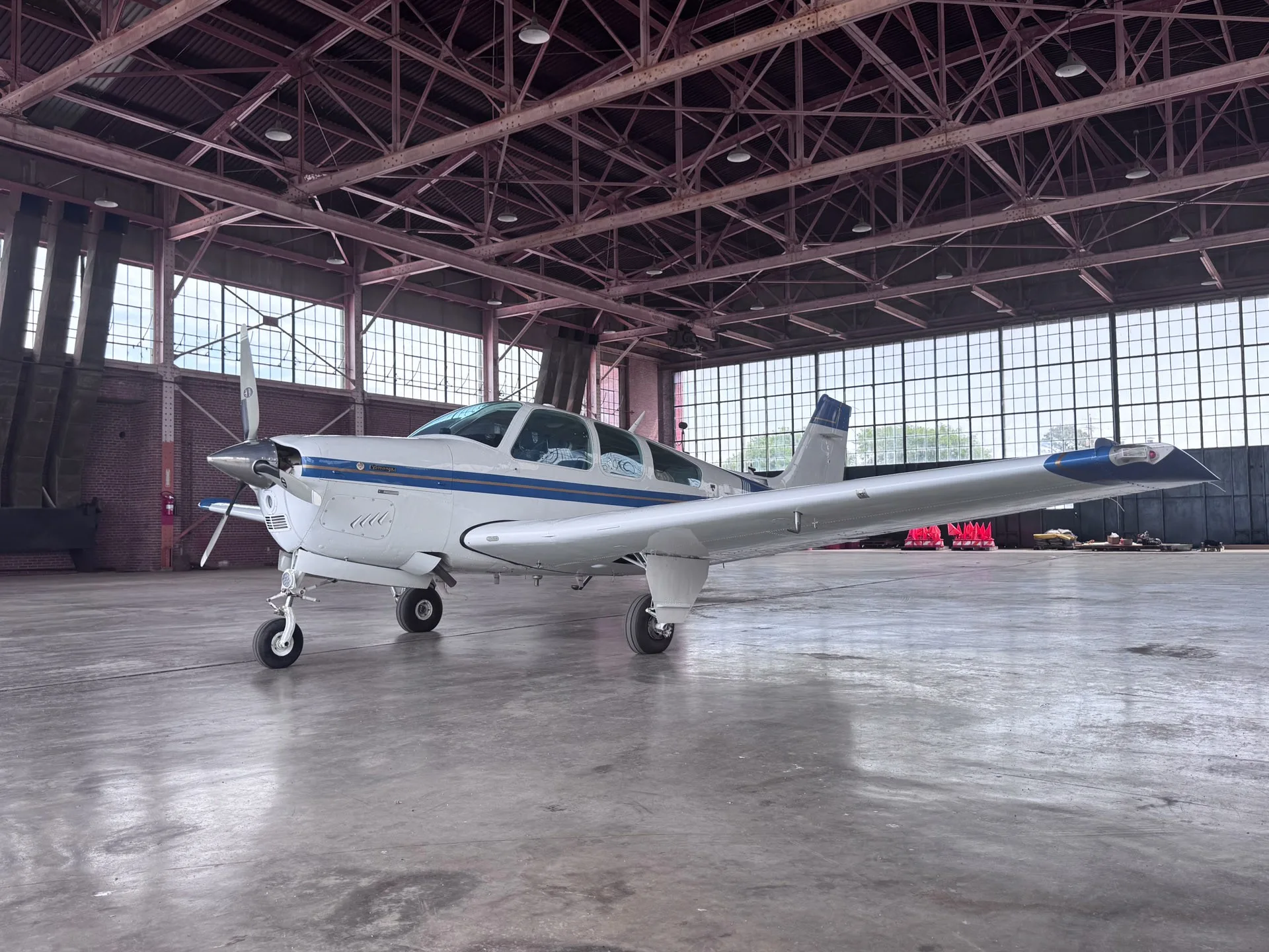 A white single-engine propeller aircraft with blue stripes parked inside a large hangar.