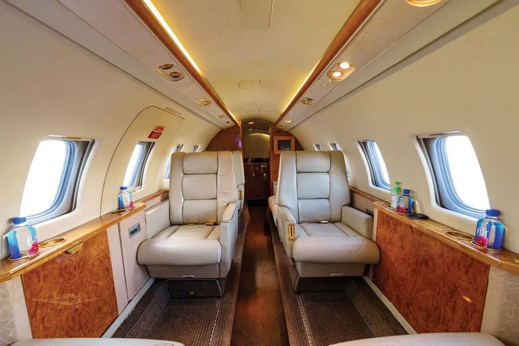 The luxurious cabin interior of the Dassault Falcon 50 features two rows of beige leather seats facing each other, with polished wood accents and large windows.