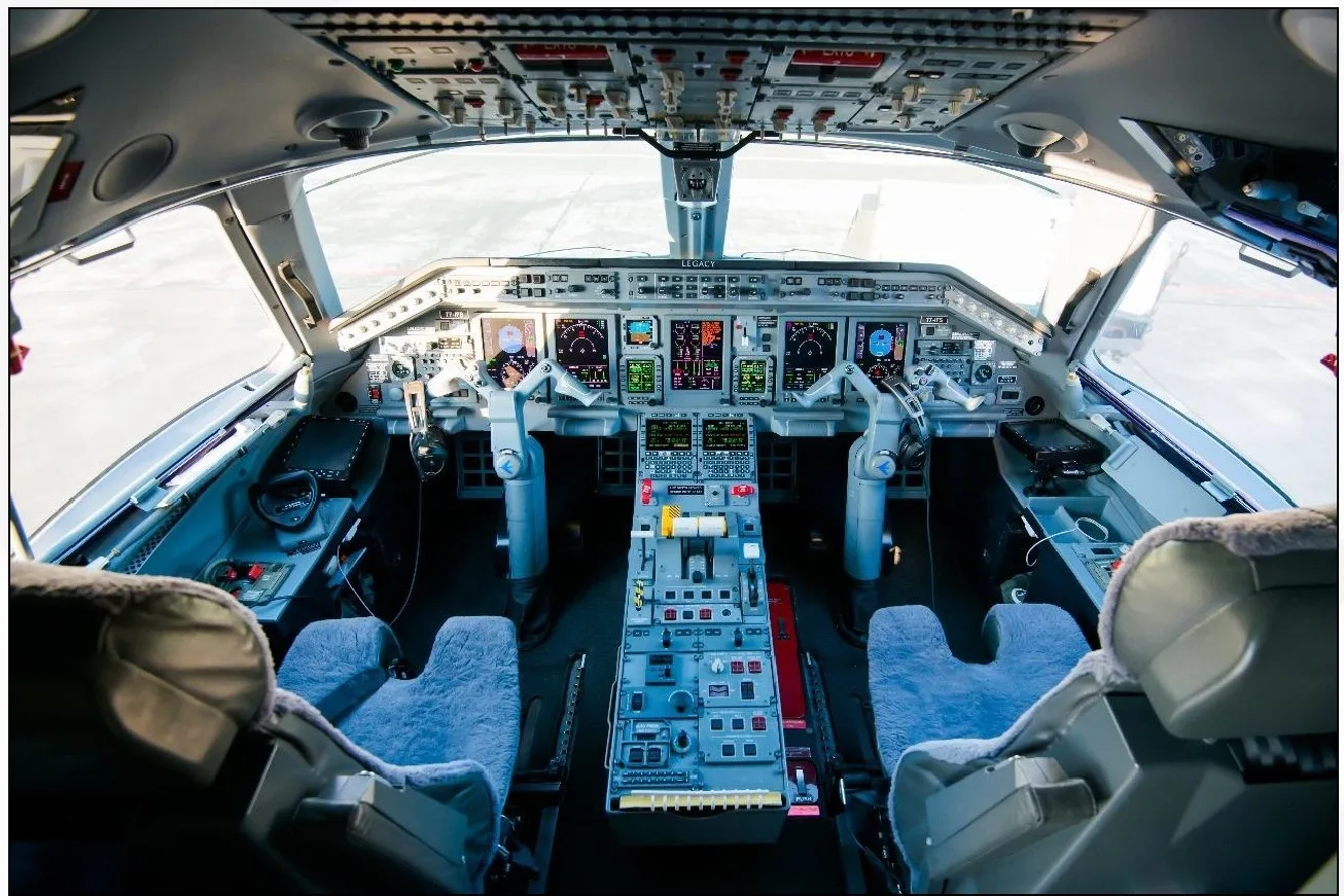 The spacious cockpit of a private jet, featuring multiple digital displays, control yokes, and a central throttle quadrant.