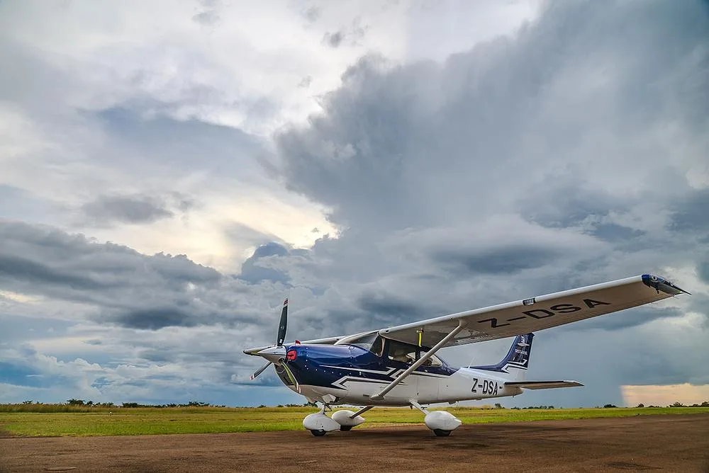 A blue and white Cessna Skylane (Z-DSA) parked on a tarmac under a dramatic cloudy sky.