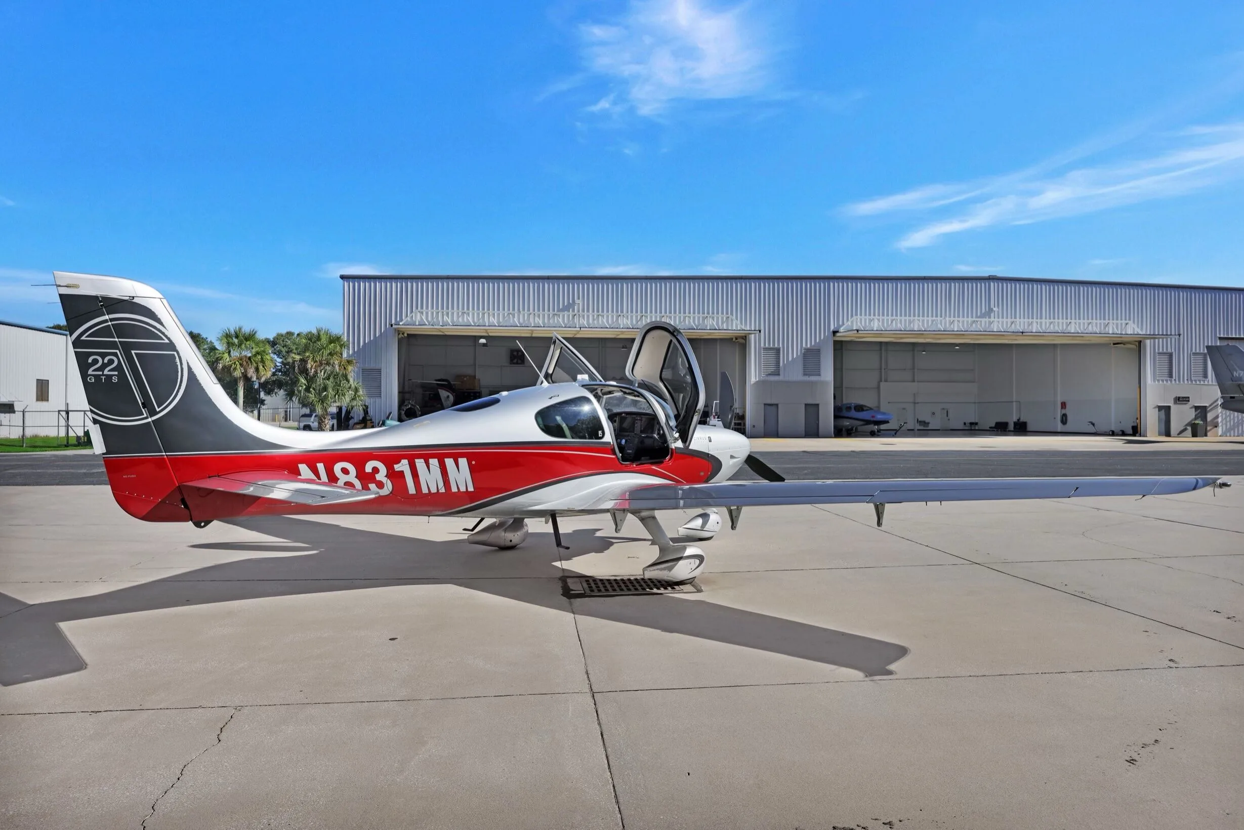 A Cirrus SR22T aircraft with red and silver paint scheme, registration N831MM, parked on an airfield with doors open.