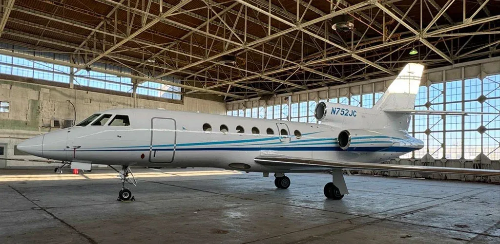 A white business jet with blue and teal stripes, registration N752JC, parked inside a hangar.