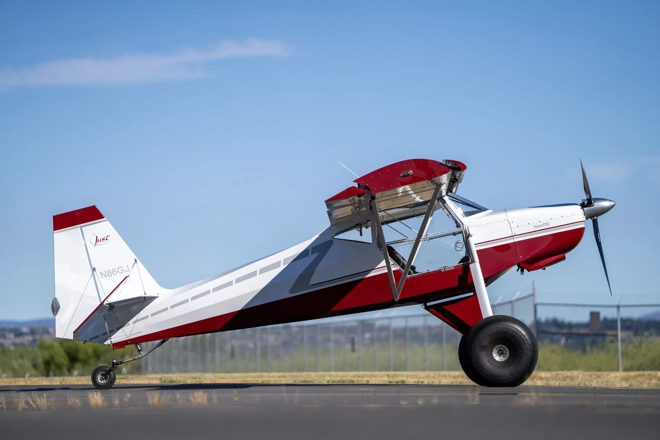 Right side view of a red and white Just Aircraft SuperSTOL with large tundra tires on an airfield.
