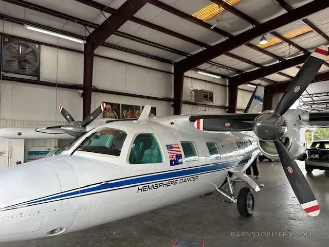 A white twin-engine turboprop aircraft with 'HEMISPHERE DANCER' text and US/Australian flags on its fuselage, parked in a hangar.