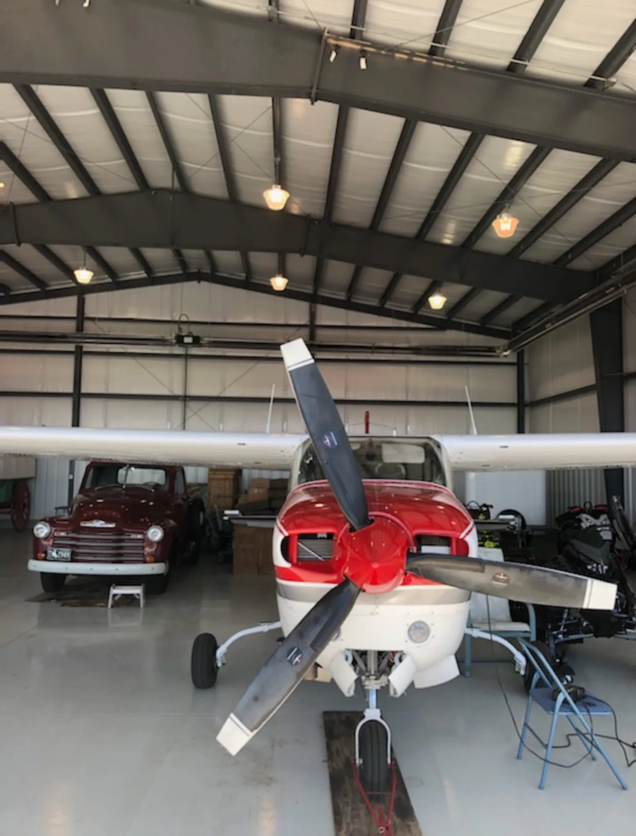 Front view of a red and white propeller aircraft inside a hangar with a vintage truck.