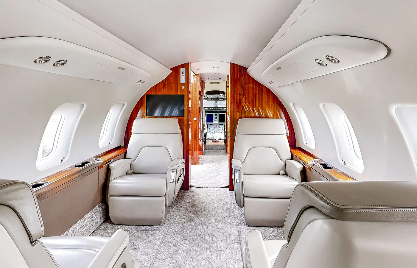 The spacious private jet cabin interior shows rows of beige leather seats and large windows.