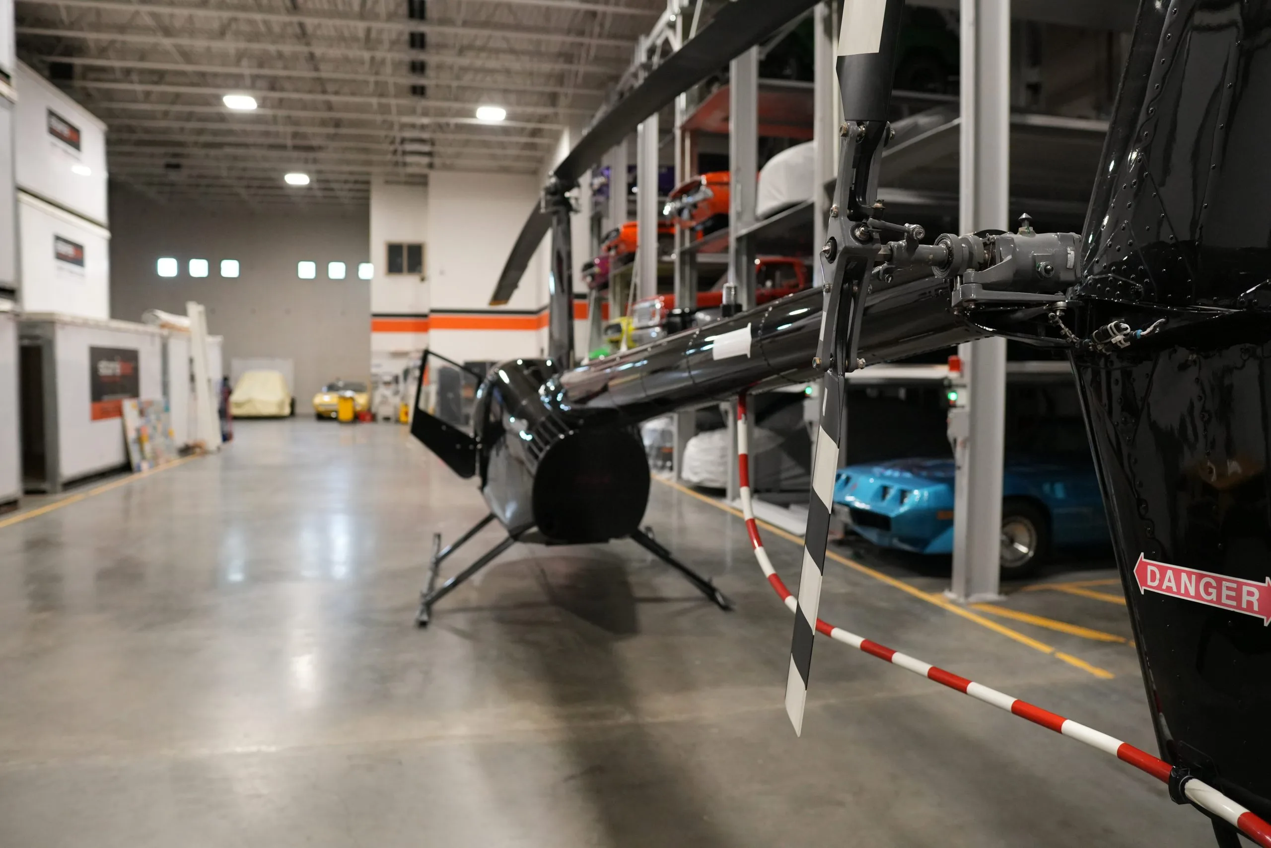 A rear view of the black Robinson R44 helicopter in a hangar, showing the tail rotor and main rotor.