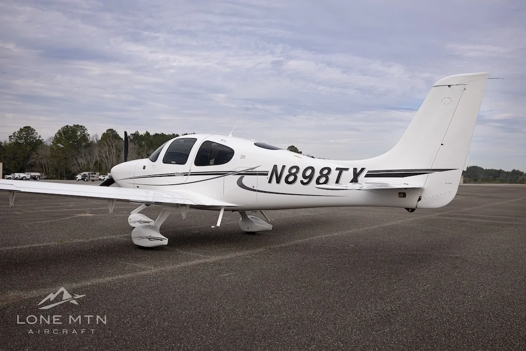 A white Cirrus SR20 aircraft with black and grey stripes, registration N898TX, viewed from the right side on an asphalt runway.