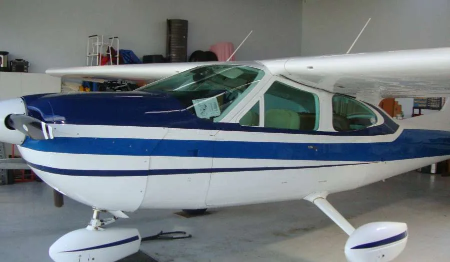 Front-left view of a white and blue single-engine aircraft with a propeller, partially inside a hangar.