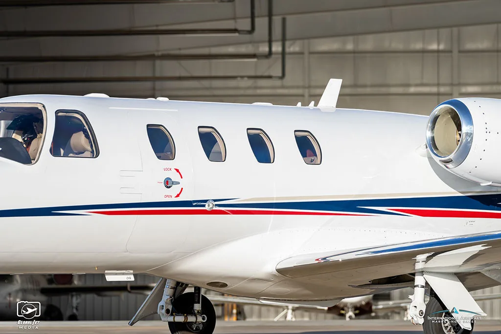 A close-up side view of the fuselage of a white Cessna Citation CJ3 with blue and red stripes.