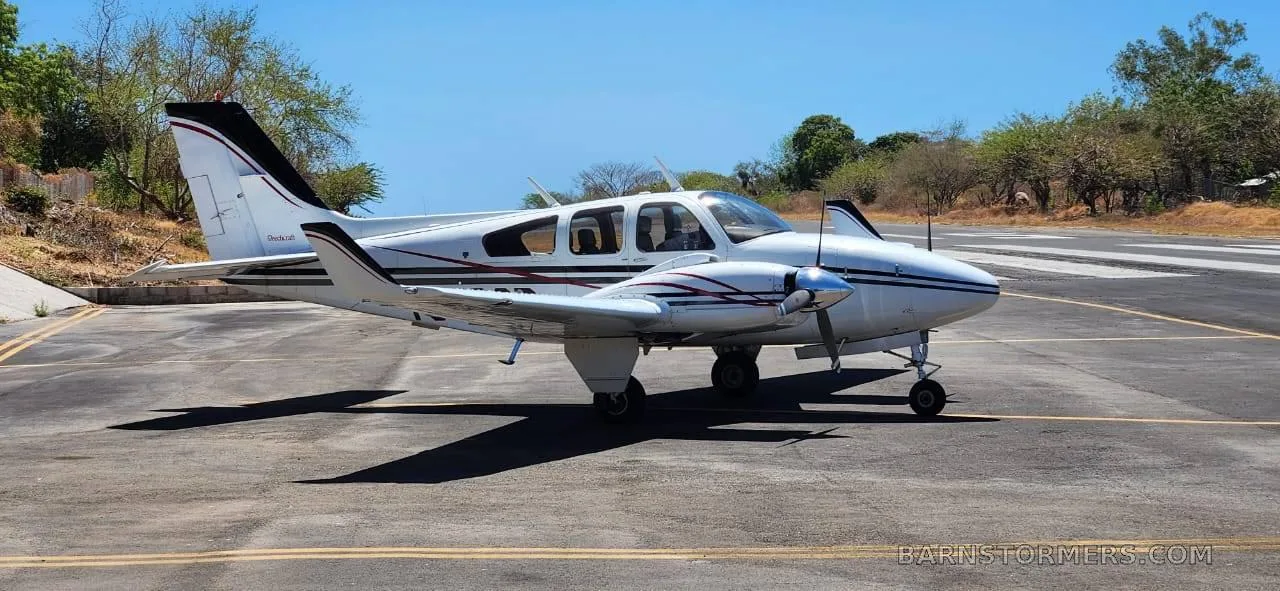 A white twin-engine aircraft with black and red stripes is parked on an asphalt tarmac under a clear blue sky.