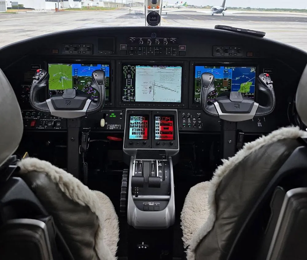 The modern glass cockpit of a Cessna Citation M2 jet, featuring multiple large display screens and control yokes.