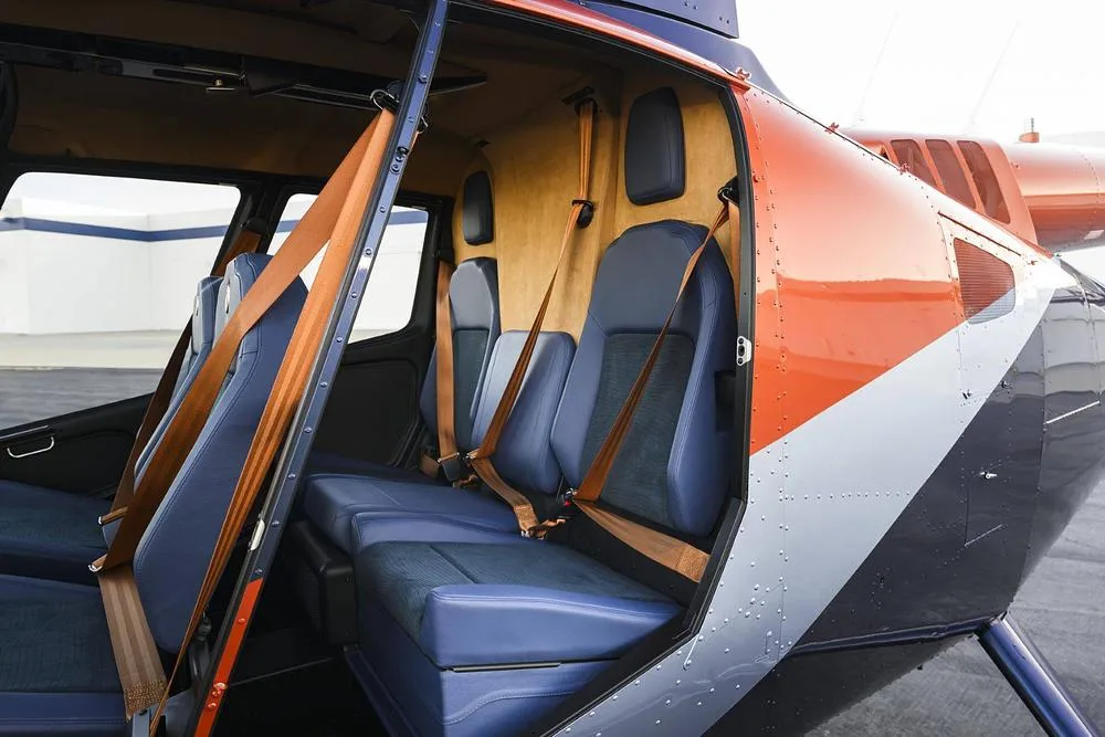 The interior of a helicopter cabin with blue seats and brown seatbelts, viewed through an open door.