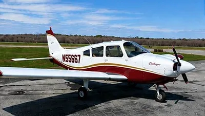 A white and red single-engine propeller aircraft, N55667, with a gold stripe, parked on a tarmac under a blue sky.