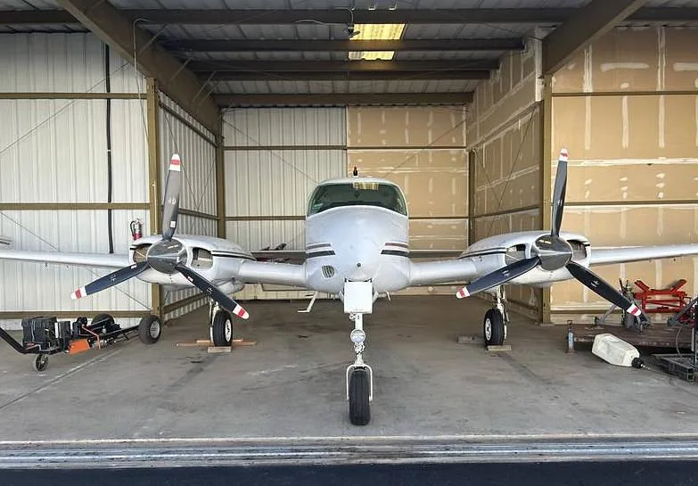 A white twin-engine propeller aircraft parked inside a hangar, viewed from the front.