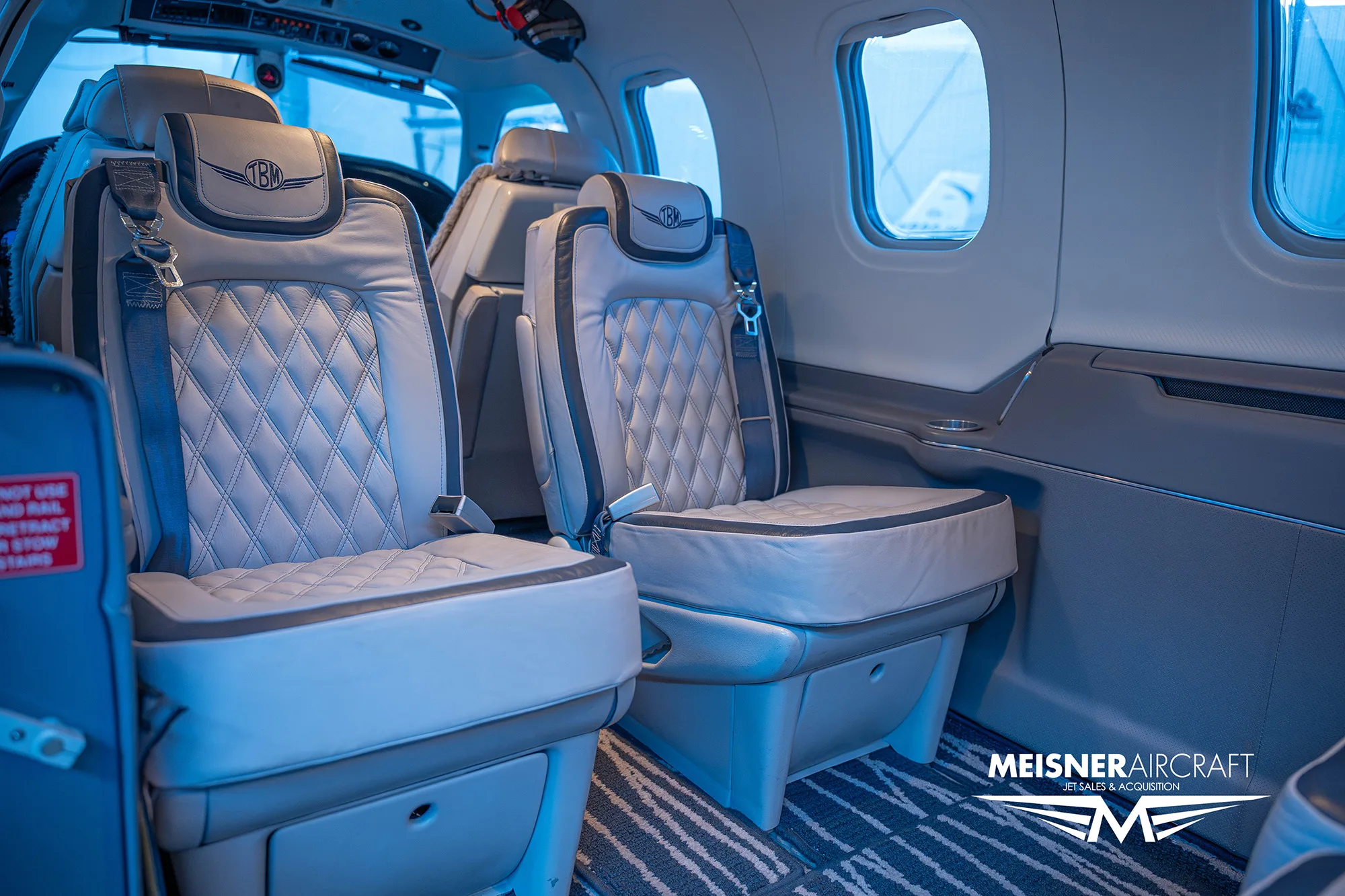 The luxurious interior cabin of an aircraft, showing two quilted leather seats with the TBM logo on the headrests.